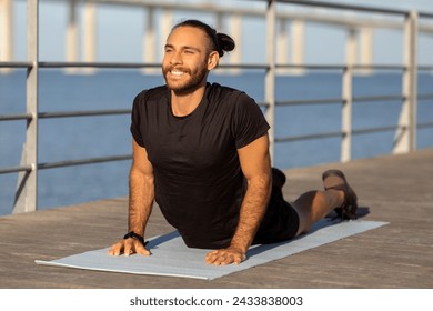 Happy athletic guy in sportswear stretching back muscles in cobra pose, practicing yoga by the sea outside, exercising on fitness mat. Flexibility, wellness and fit lifestyle - Powered by Shutterstock