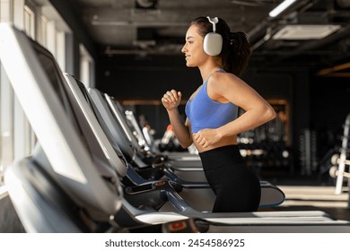 Happy athletic lady wearing wireless headphones while jogging on running track in sport gym, enjoying workout with music - Powered by Shutterstock