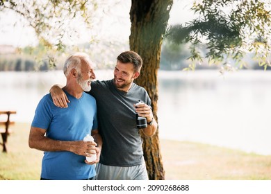 Happy athletic man and his mature father talking while drinking water and walking after sports training in nature. Copy space. - Powered by Shutterstock