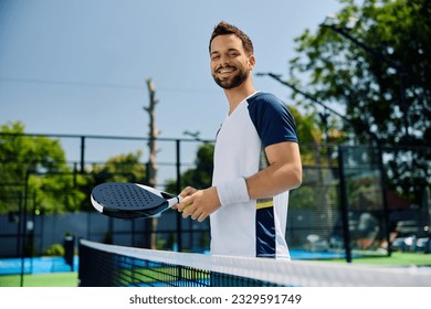 Happy athletic man playing padel on outdoor court and looking at camera. - Powered by Shutterstock