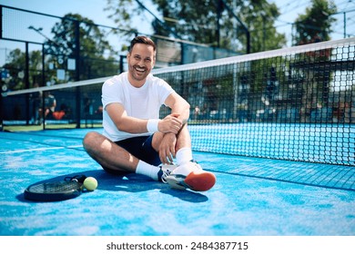 Happy athletic man relaxing on paddle tennis court and looking at camera. Copy space.  - Powered by Shutterstock