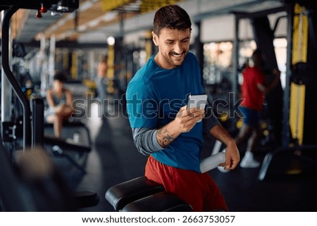 Happy athletic man using app on cell phone during gym workout. Copy space. 