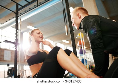 Happy athletic woman doing curl up exercise at the gym with the help of her personal trainer. Fitness female doing sit ups with man holding her feet. - Powered by Shutterstock