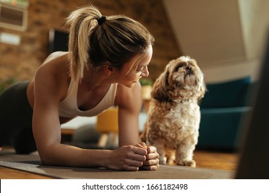 Happy Athletic Woman Doing Plank Exercise While Her Dog Is Sitting Next To Her. 