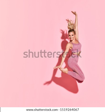 Happy athletic woman jumping in silhouette. Photo of sporty woman in fashionable pink sportswear on pink background. Sport and healthy lifestyle. Dynamic movement.