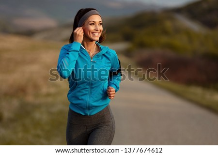 Happy athletic woman listening music on earphones while running in nature in the morning. Copy space. 