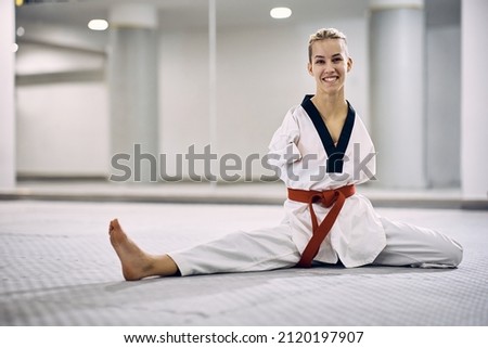 Happy athletic woman with para-ability stretching on the floor during taekwondo training in health club and looking at camera. 