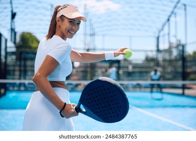 Happy athletic woman serving the ball while playing paddle tennis and looking at camera.  - Powered by Shutterstock