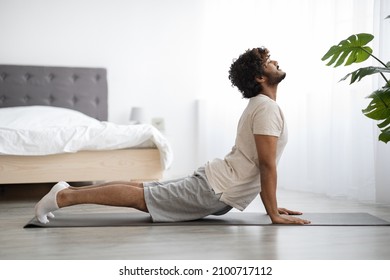 Happy athletic young indian man in sportswear stretching his body at home, sporty dark-skinned guy enjoying yoga practice, side view, copy space. Healthy lifestyle, sport while pandemic concept - Powered by Shutterstock