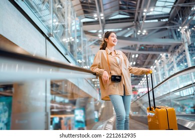 Happy attractive asian woman traveler with a yellow suitcase at the modern airport terminal, copy space, Tourist journey trip concept