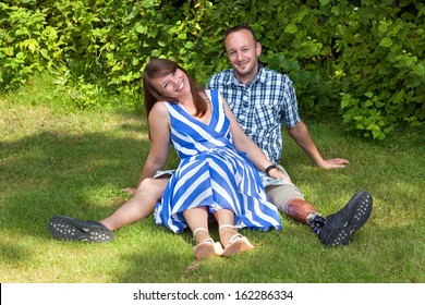 Happy attractive couple relaxing in the garden sitting close together on the grass with joyful friendly smiles - the man is disabled and is wearing a prosthetic artificial leg - Powered by Shutterstock