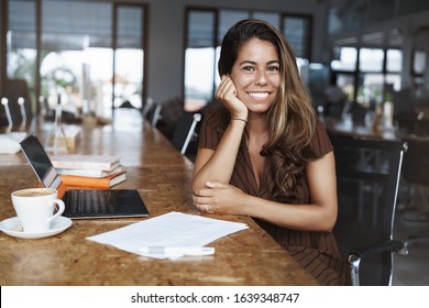 Happy, Attractive Female Entrepreneur, Take Coffee Break In Cafe Near Office, Write Down Notes, Read Documents, Drink Cappuccino And Use Laptop As Work Remote. Digital Nomad, Gig Economy Concept