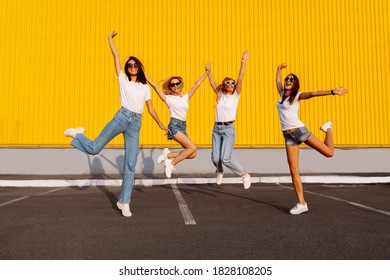 Happy attractive female friends jumping and having fun on a summer sunny day, against the background of a yellow wall of a shopping center, friendship concept