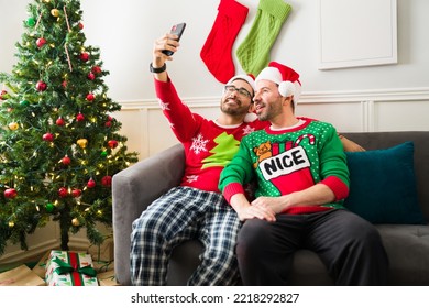 Happy attractive gay couple wearing pajamas and santa hats taking a selfie for social media while celebrating christmas - Powered by Shutterstock