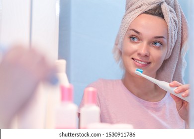Happy attractive healthy woman brush teeth using ultrasonic electric toothbrush in bathroom at home. Oral hygiene, dental and gum health, healthy teeth. Daily life and routine