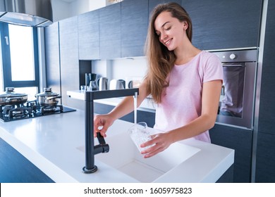 Happy attractive joyful brunette woman pours fresh clean filtered purified water for drinking from a tap into a glass at kitchen at home. Healthy lifestyle  - Powered by Shutterstock