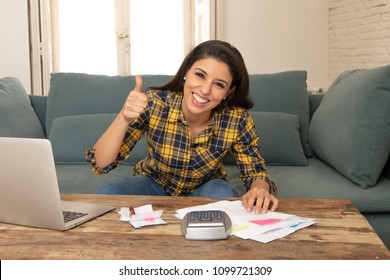 Happy Attractive Latin Woman Calculating Home Finances And Paying Bills At Home Using Calculator And Laptop With Her Thumb Up.