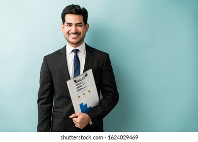 Happy Attractive Male Executive Holding Clipboard With Chart While Standing Against Colored Background