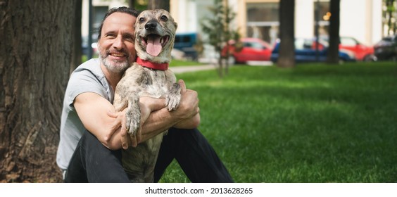 Happy attractive mature man 50 years old resting on the grass while walking with his dog - Powered by Shutterstock