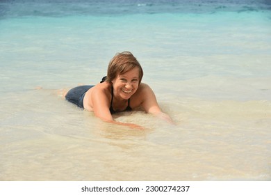 Happy attractive mature woman 50-60 lies in the water on the beach. Senior woman wear black swimsuit. Concept - travel, retirement, active elderly people, Philippines - Powered by Shutterstock