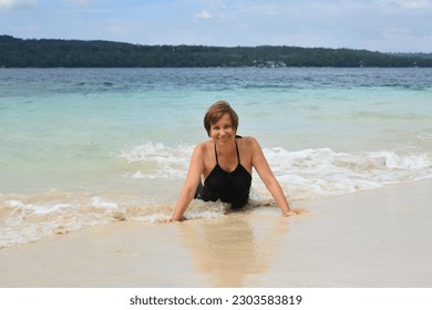 Happy attractive mature woman 50-60 lies in the water on the beach. Senior woman wear black swimsuit. Concept - travel, retirement, active elderly people, Philippines - Powered by Shutterstock