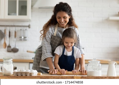 Happy attractive mommy helping cute smiling little preschool child daughter rolling dough for homemade pastry. Excited two female generations family enjoying cooking process together in kitchen. - Powered by Shutterstock