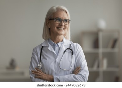 Happy attractive older attending physician in white coat posing in clinic office, smile, look into distance, feel satisfied with workday and professional aid to patients. Mission, profession, medicine - Powered by Shutterstock