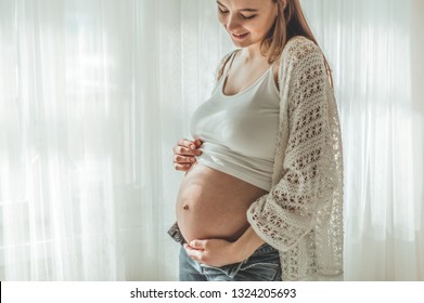 Happy Attractive pregnant woman standing near the window and holding her belly. Concepts of pregnancy and family