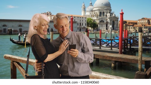 Happy And Attractive Senior Couple Using Smartphone In Venice