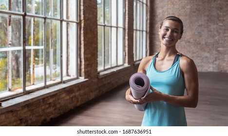 Happy attractive sporty fit young woman yoga class training instructor personal fitness trainer wear sportswear holding rolled yoga mat standing in gym looking at camera, portrait banner copy space - Powered by Shutterstock