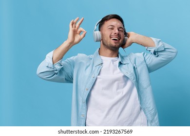 Happy attractive tanned handsome man in casual basic t-shirt headphones listen cool sound show gesture Okay posing isolated on blue studio background. Copy space Banner Mockup. Music concept - Shutterstock ID 2193267569