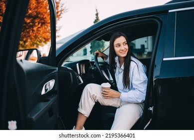 Happy attractive woman or business lady wearing eyeglasses holding cup of coffee and getting out of her modern car - Shutterstock ID 2195366401