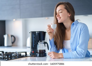 Happy Attractive Woman Enjoying Of Fresh Coffee Aroma After Brewing Coffee Using Coffee Maker In The Kitchen At Home. Coffee Blender And Household Kitchen Appliances For Makes Hot Drinks