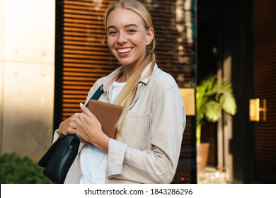 Happy attractive woman walking in the street, carrying bag and diary