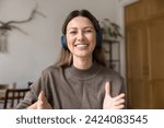 Happy attractive woman in wireless headphones speaking at camera with toothy smile and moving hands, talking on video call, laughing. Online conference chat screen head shot portrait