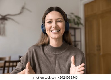 Happy attractive woman in wireless headphones speaking at camera with toothy smile and moving hands, talking on video call, laughing. Online conference chat screen head shot portrait - Powered by Shutterstock