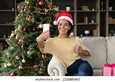 Happy attractive young african ethnicity biracial woman in festive mood recording video in social network on cellphone, with glass of sparkling wine in hands, celebrating New Year Christmas at home. - Powered by Shutterstock