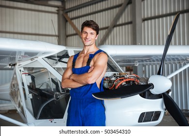 Happy Attractive Young Aircraft Mechanic Standing With Arms Crossed Near Small Airplane