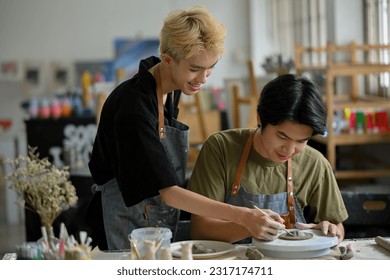 A happy and attractive young Asian gay man holds his boyfriend's hand to create shapes on raw clay, enjoying molding clay in the workshop together. - Powered by Shutterstock