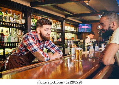 Happy Attractive Young Barman Giving Glass Of Beer And Talking To African American Young Man 