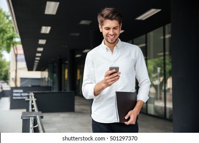 Happy attractive young businessman walking and using mobile phone outdoors - Powered by Shutterstock