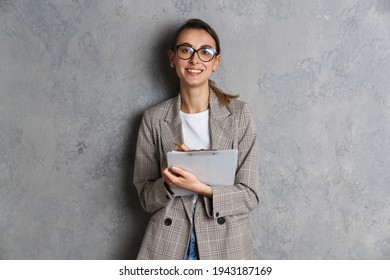 Happy attractive young casual woman taking notes while standing isolated over background