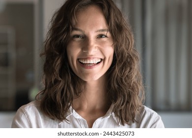 Happy attractive young Caucasian woman with wavy hair looking at camera with toothy smile, laughing, posing for front close up portrait. Cheerful successful professional girl video call head shot - Powered by Shutterstock