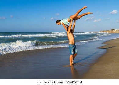 Happy attractive young couple in bikini and shorts enjoying summer dusk at the beach, doing fitness exercises, having fun walking barefoot, kissing and teasing one another. - Shutterstock ID 346429454