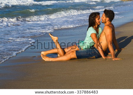 Happy attractive young couple in bikini and shorts enjoying summer dusk at the beach, practicing fitness exercises, having getting wet, kissing and teasing one another.