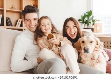 Happy attractive young family hugging at cozy home. Portrait smiling father, mother, cute little daughter and golden retriever dog  looking at camera sitting on comfortable sofa. Love, parenthood  - Powered by Shutterstock