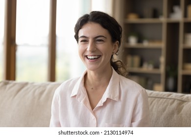 Happy Attractive Young Hispanic Woman Sitting On Sofa, Looking Away, Watching Funny Comedian Movie Or TV Series Or Communicating Sitting On Couch At Home, Feeling Relaxed On Weekend Indoors.