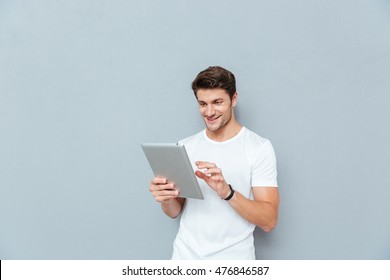 Happy attractive young man standing and using tablet over grey background - Powered by Shutterstock