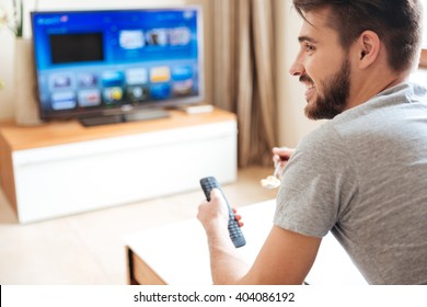 Happy Attractive Young Man Watching Tv And Using Remote Control At Home 