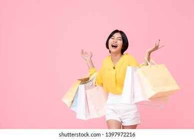 Happy Attractive Young Thai Asian Female Carrying Pastel Colored Shopping Bags With Both Arms Raised In A Ecstatic Gesture Isolated In Pink Studio Background